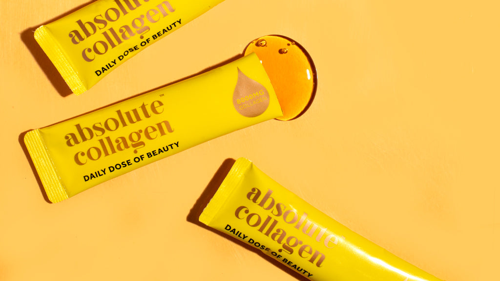 Foto von Absolute Collagen Beutel auf einem orangenen Hintergrund. Ein Beutel ist aufgerissen und Flüssigkeit kommt daraus